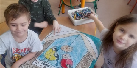 Powiększ grafikę: dzieci prezentują wspólną pracę dotyczącą dokarmiania ptaków na obrazku dzieci wróbel i sikorka