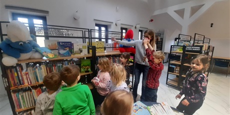 Powiększ grafikę: grupa dzieci przy bibliotecznych półkach