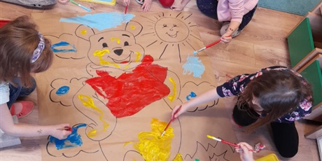 Powiększ grafikę: Grupa motylków maluje farbami plakat z Kubusiem Puchatkiem