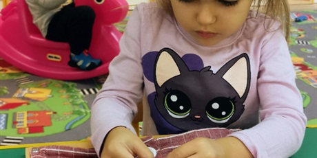 Powiększ grafikę: Kamila pracuje z ramka sensoryczną, uczy się zapinać guziki
